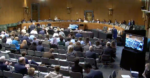 screenshot of the livestream of the senate hearing. it depicts a dais for senators at the back of the image and a hearing room of seats before them